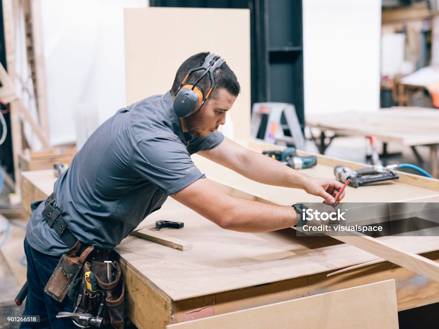 Menuisier prenant les mesures d'un plateau en atelier